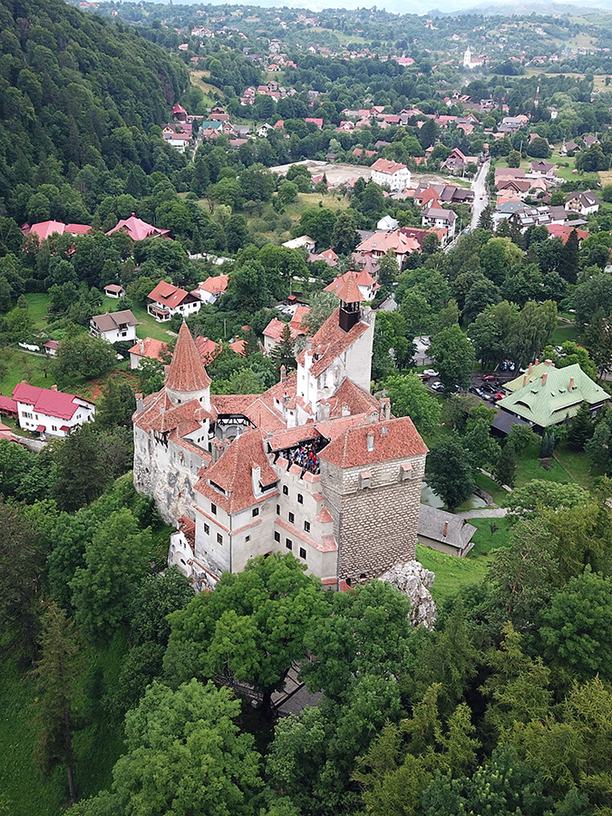 Vedere aeriană oblică de ansamblu: volumele castelului, acoperișurile, curtea și pintenul stâncos.