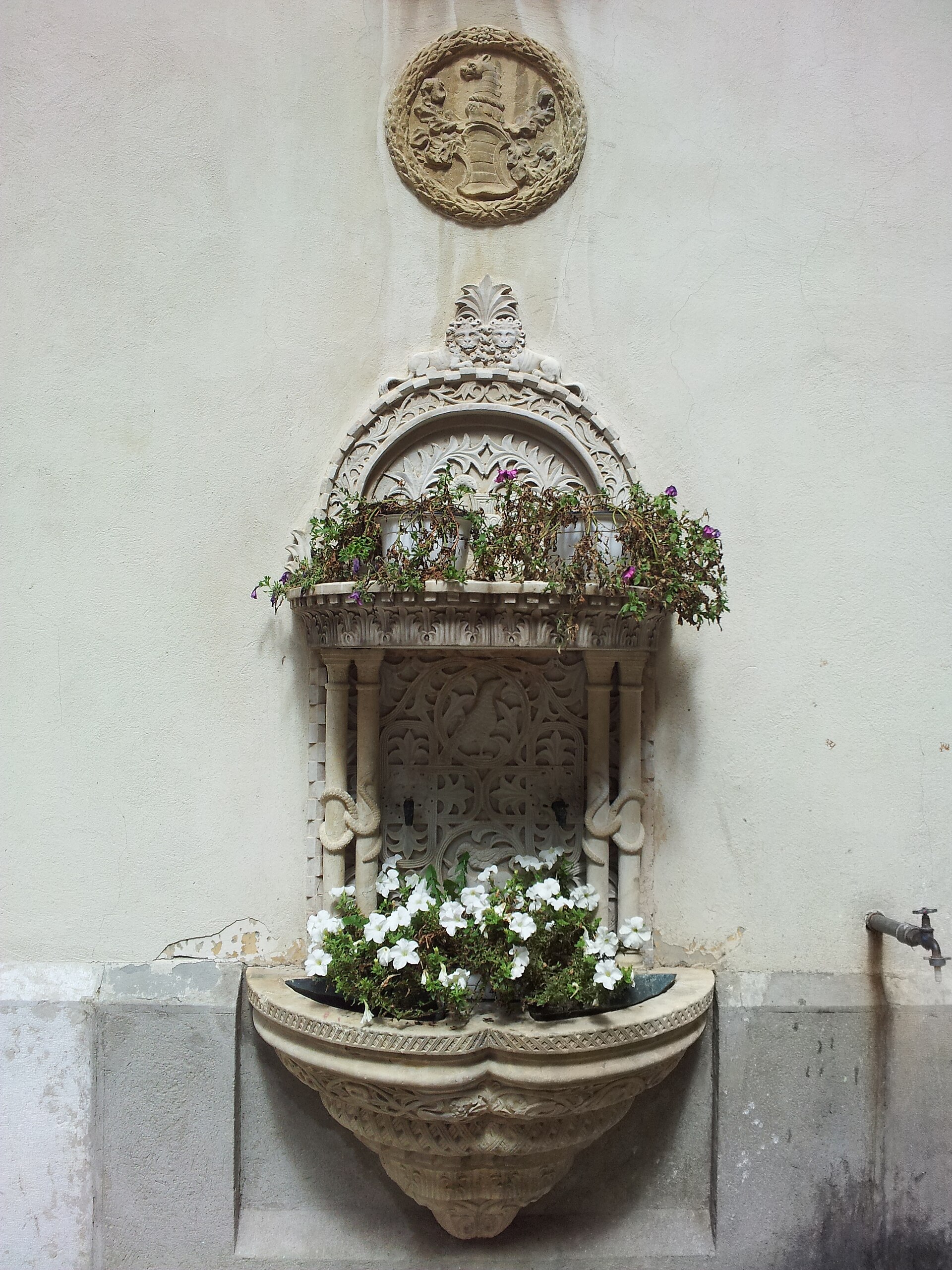 Fântâna de perete din curte, cu bazin, fronton și ornament.