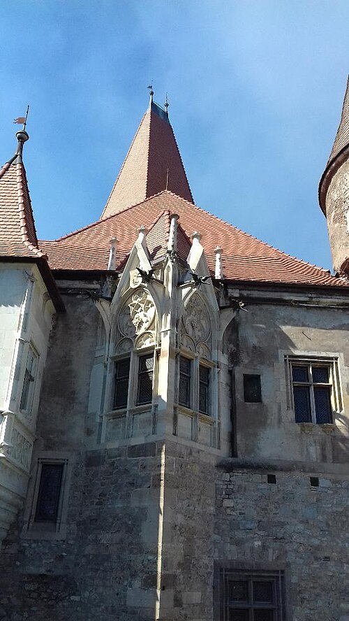 Fațadă de curte cu ferestre sculptate, fronton și turn circular alăturat.