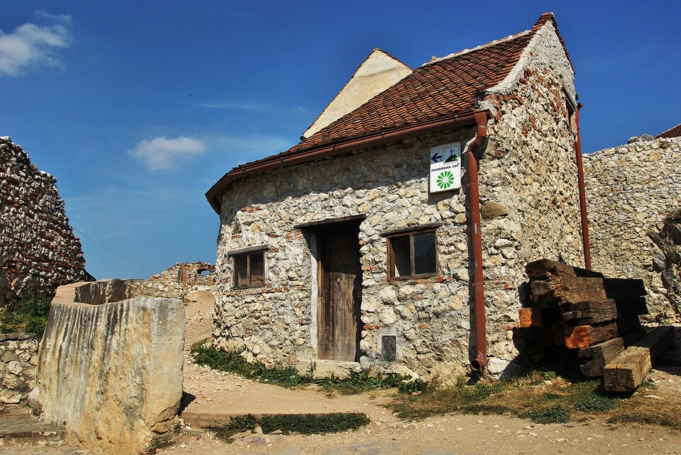 Mică construcție din piatră cu fronton, ușă, ferestre și acoperiș de țiglă.