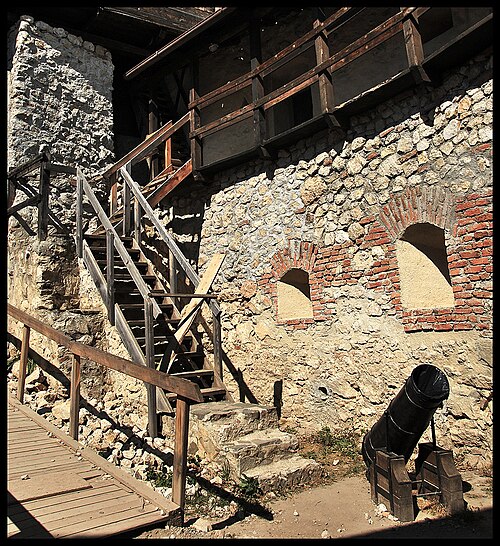 Scară exterioară și galerie de lemn deasupra zidului cu goluri arcuite.