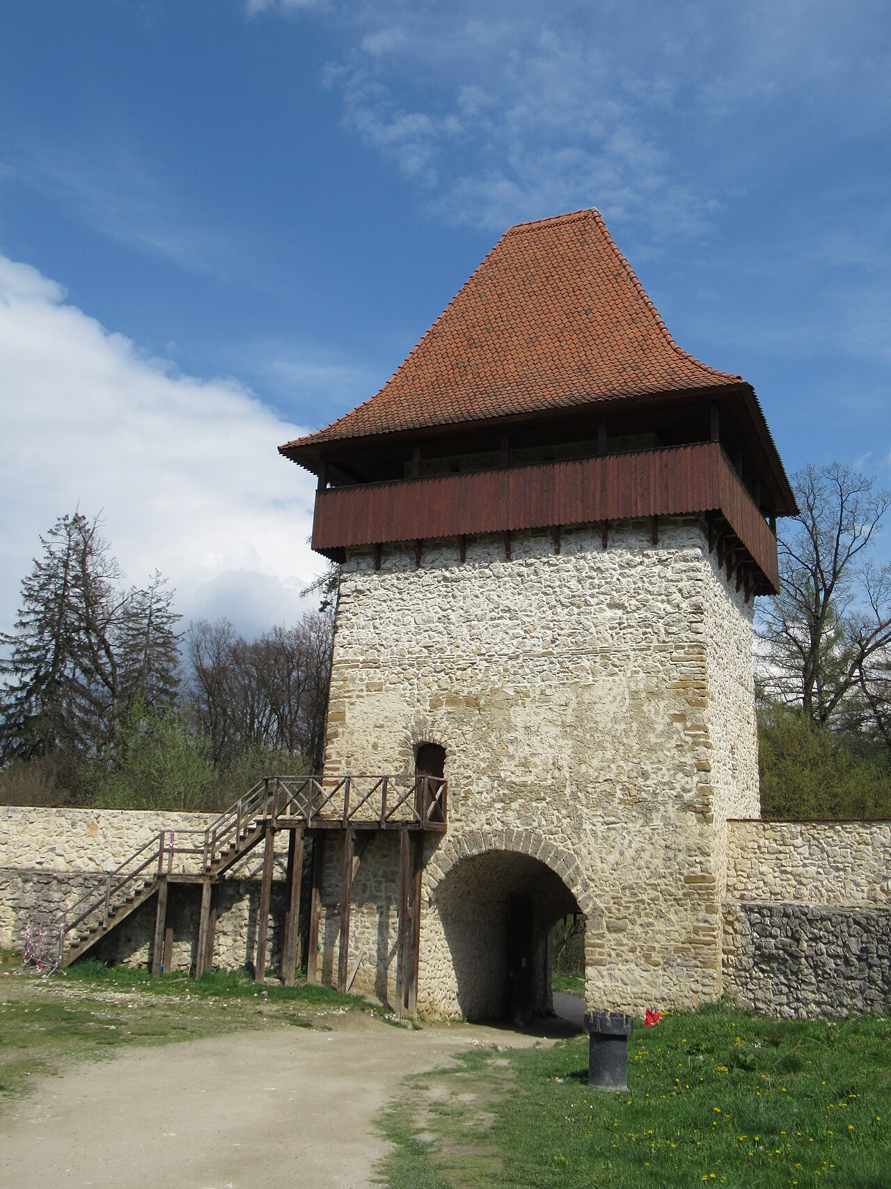 Turnul exterior privit aproape frontal: poartă, soclu, volum de lemn și streșini.