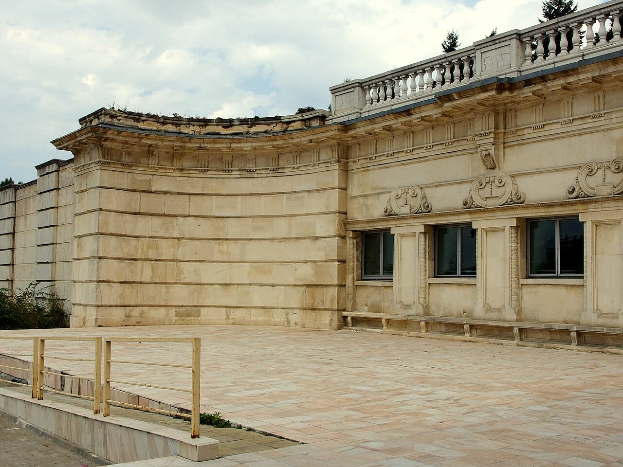 Detaliu exterior de soclu, placaj, ferestre, cornișă curbată și balustradă.