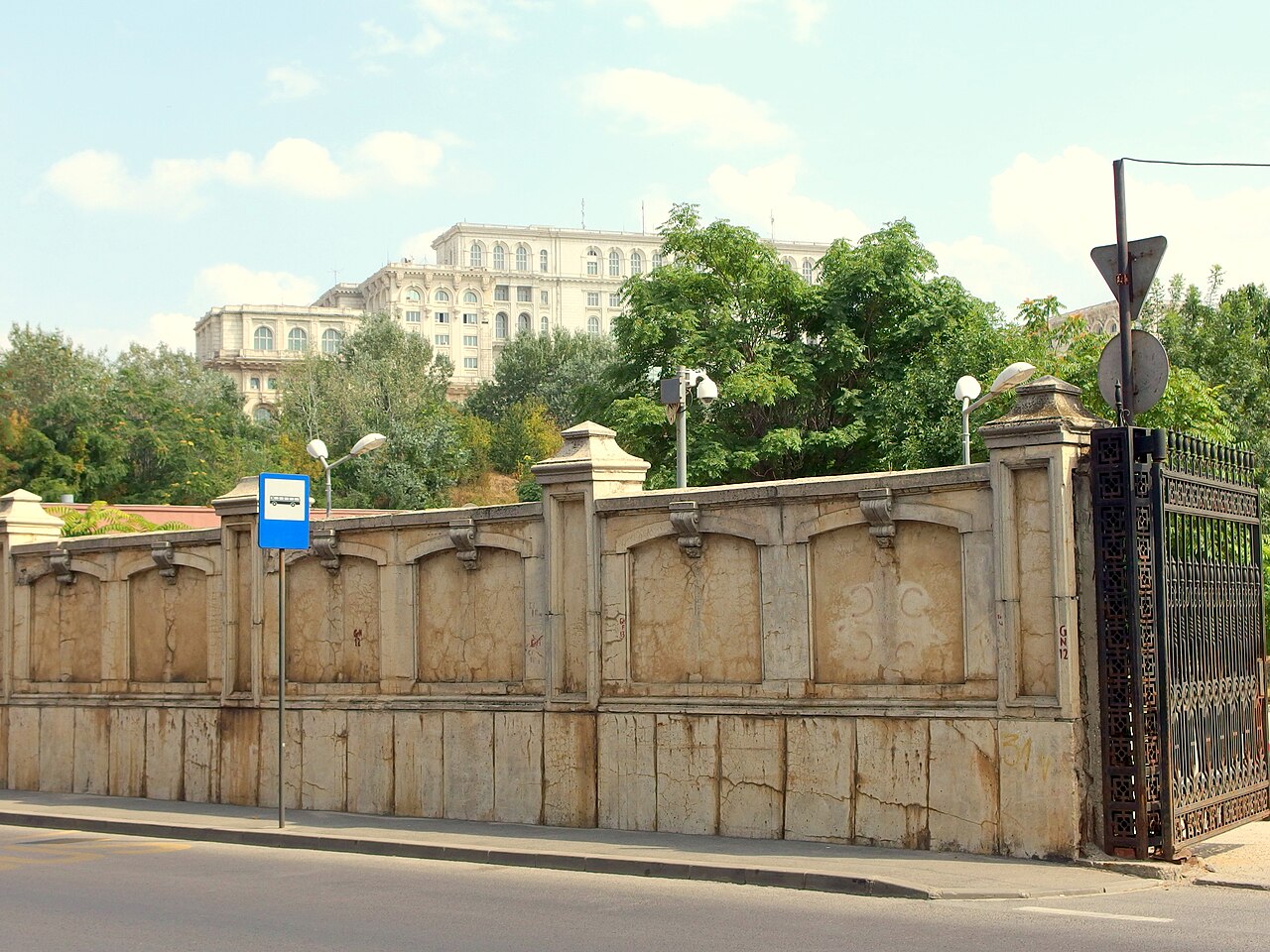 Gardul perimetral din piatră cu stâlpi și poartă, palatul în fundal.