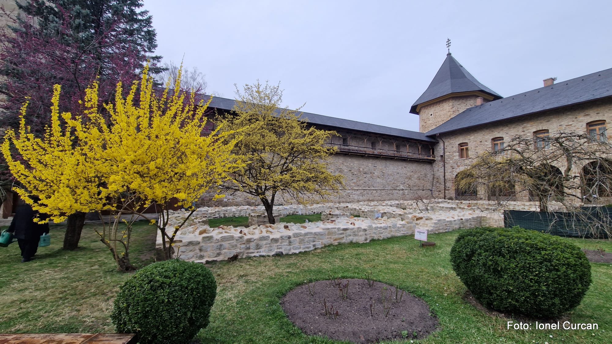Curte: galerie de lemn, zid interior și turn, văzute peste grădina amenajată