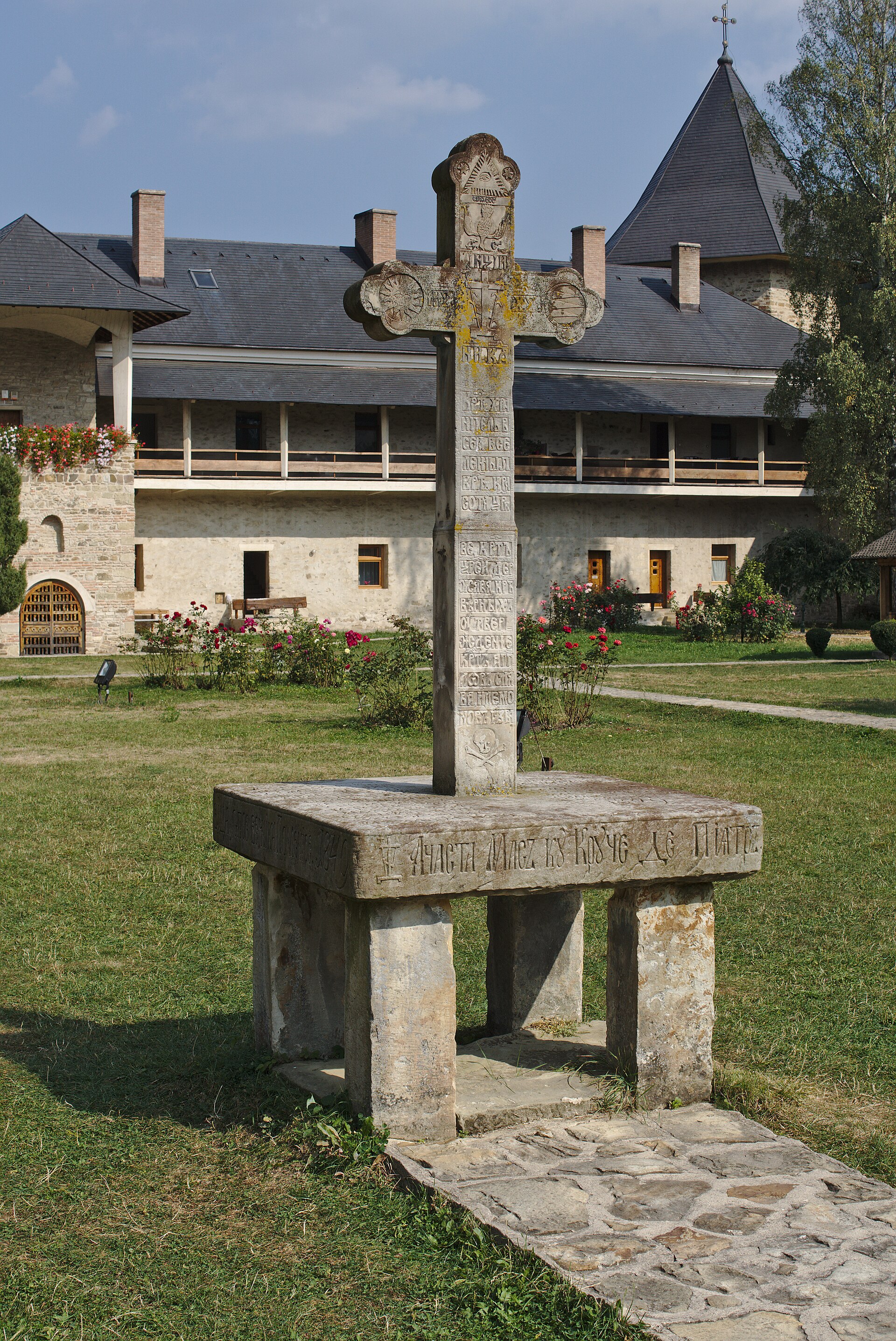 Crucea de piatră din curte și soclul, cu corpul monastic în fundal
