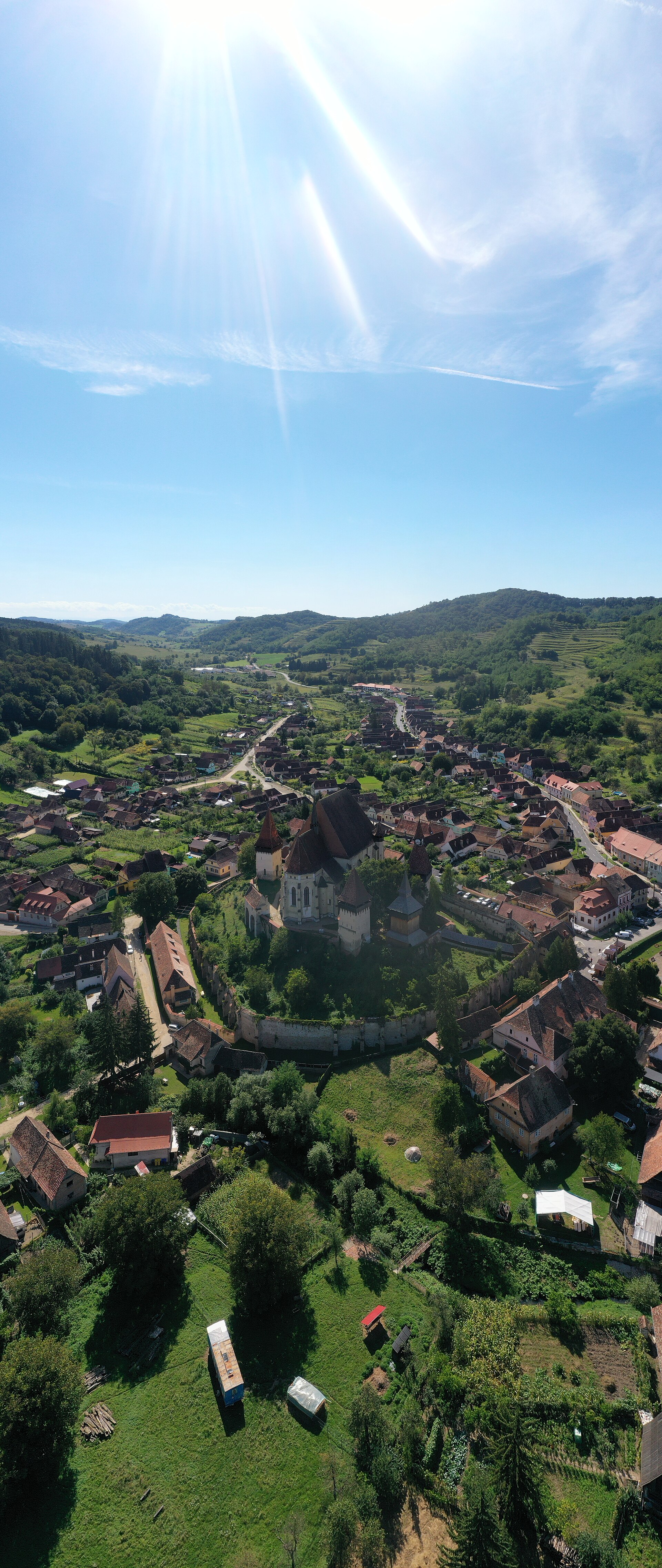 Vedere aeriană oblică a bisericii și incintelor concentrice, cu satul în jur; cadru vertical