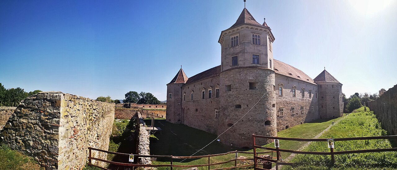 Colțul castelului și turnul, văzute oblic peste terenul curții