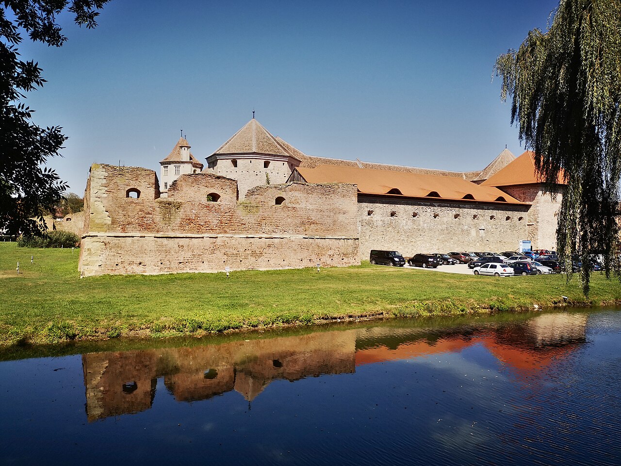 Fațada castelului și zidul exterior văzute peste apă, cu reflexie