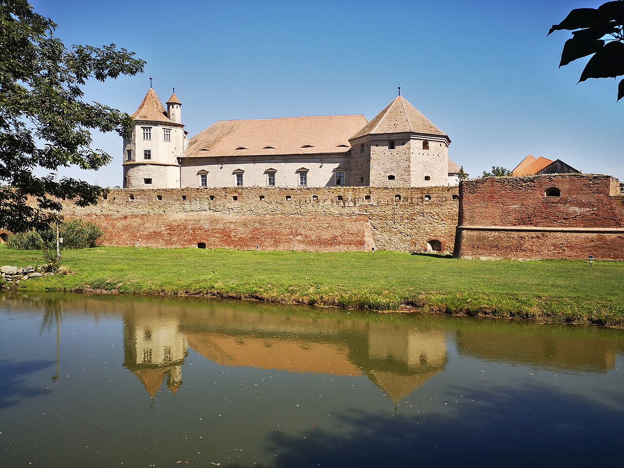 Fațadă lungă, acoperișuri și bastion văzute de pe malul șanțului