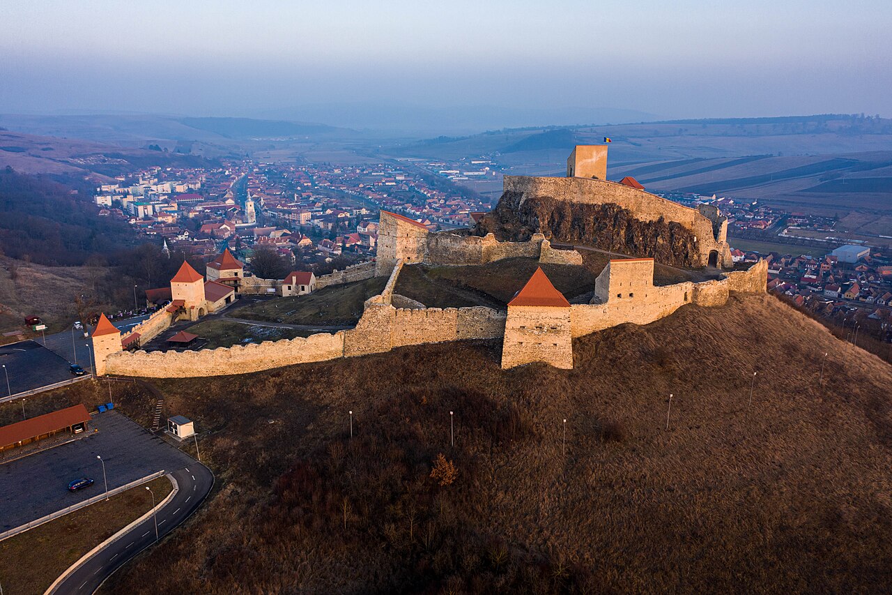 Vedere aeriană oblică la apus, cu incintele, turnurile și orașul în jur