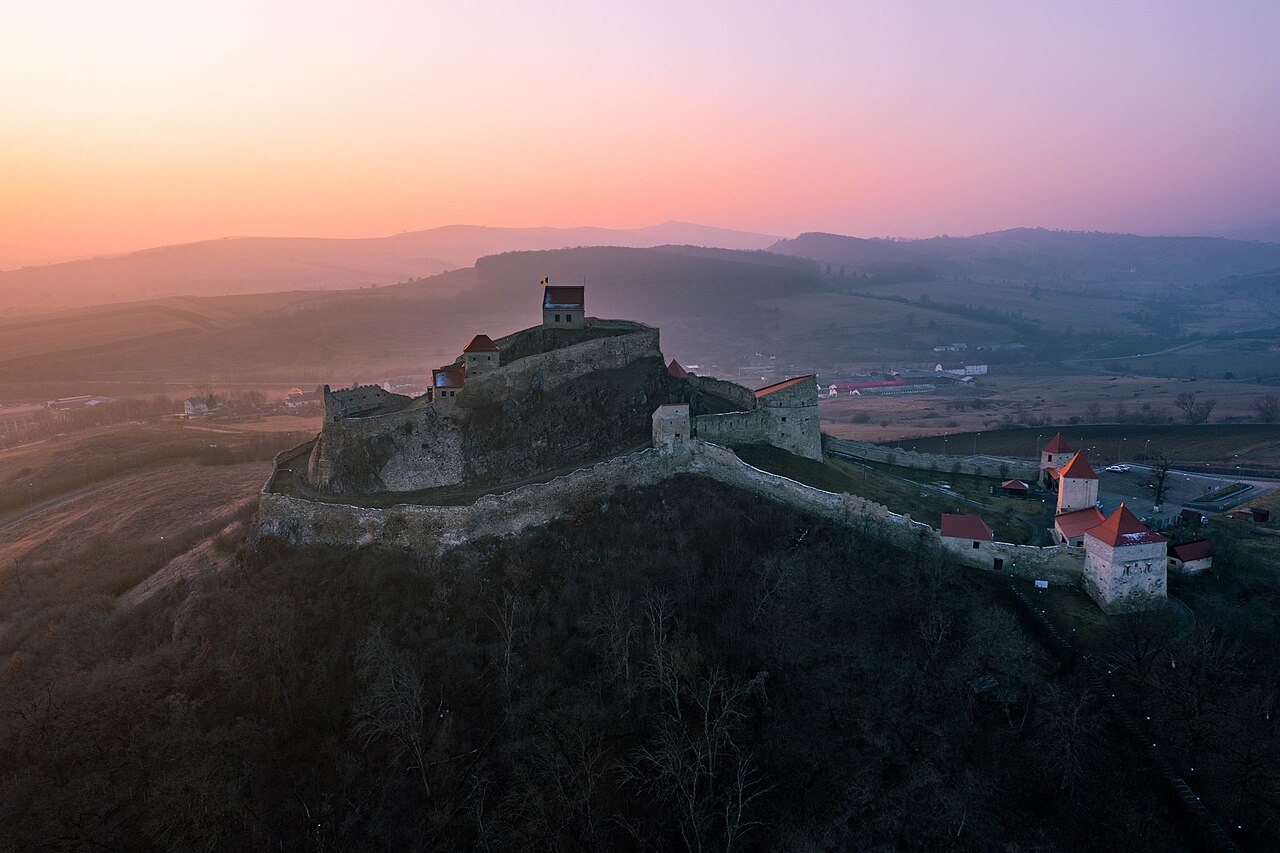 Vedere aeriană la apus dinspre latura opusă: incinte, ziduri și pante