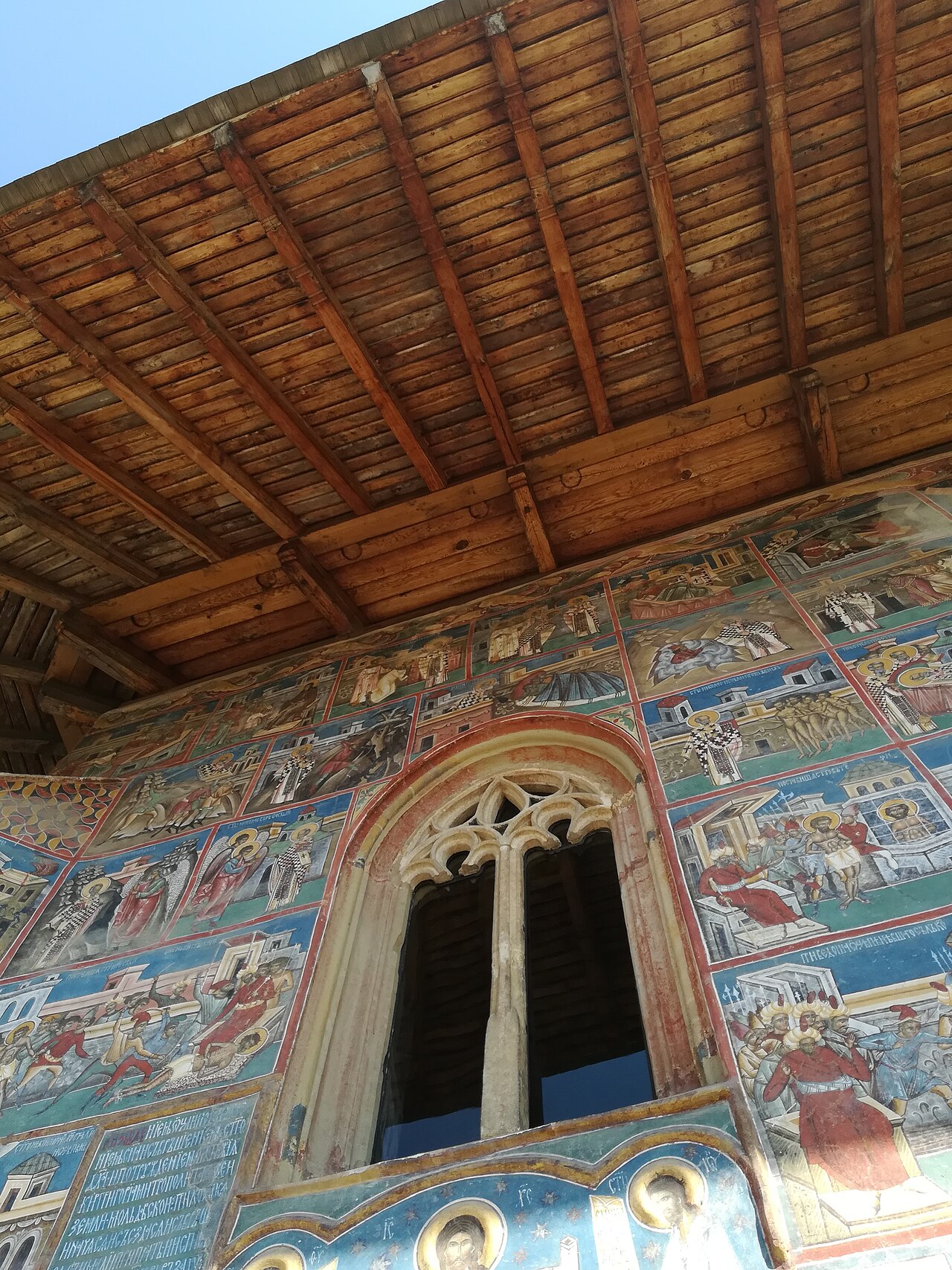 Detaliu de fereastră, pictură murală și structura de lemn de sub streașină.