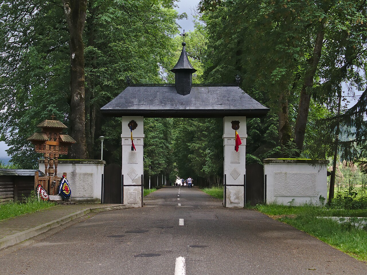 Poartă exterioară de acces, cu stâlpi albi și acoperiș.