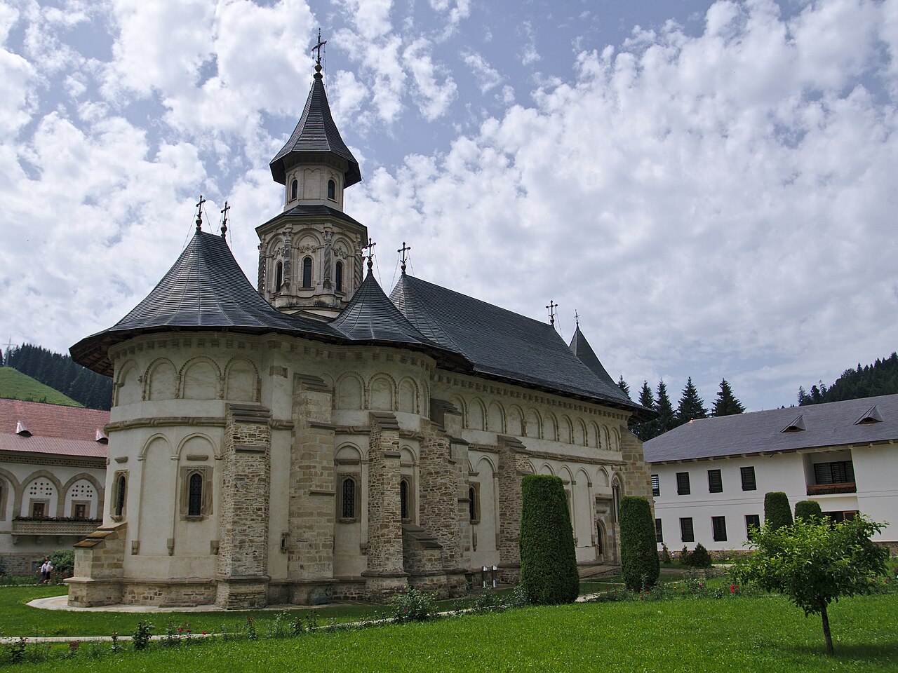 Biserica văzută din colțul complementar, cu pereții de piatră și anexele în fundal.