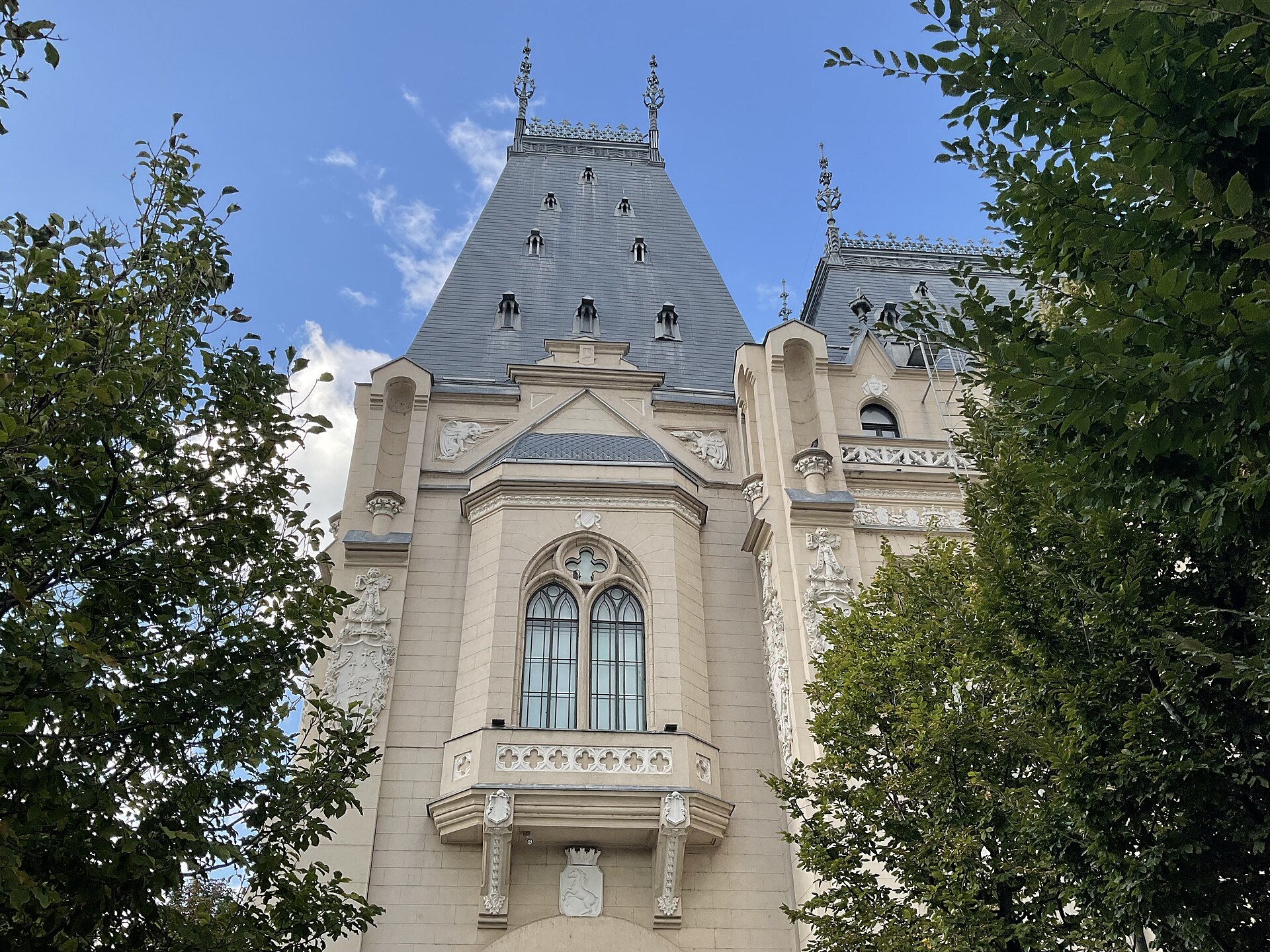 Corp înalt cu ferestre gotice și balcon, văzut prin vegetație