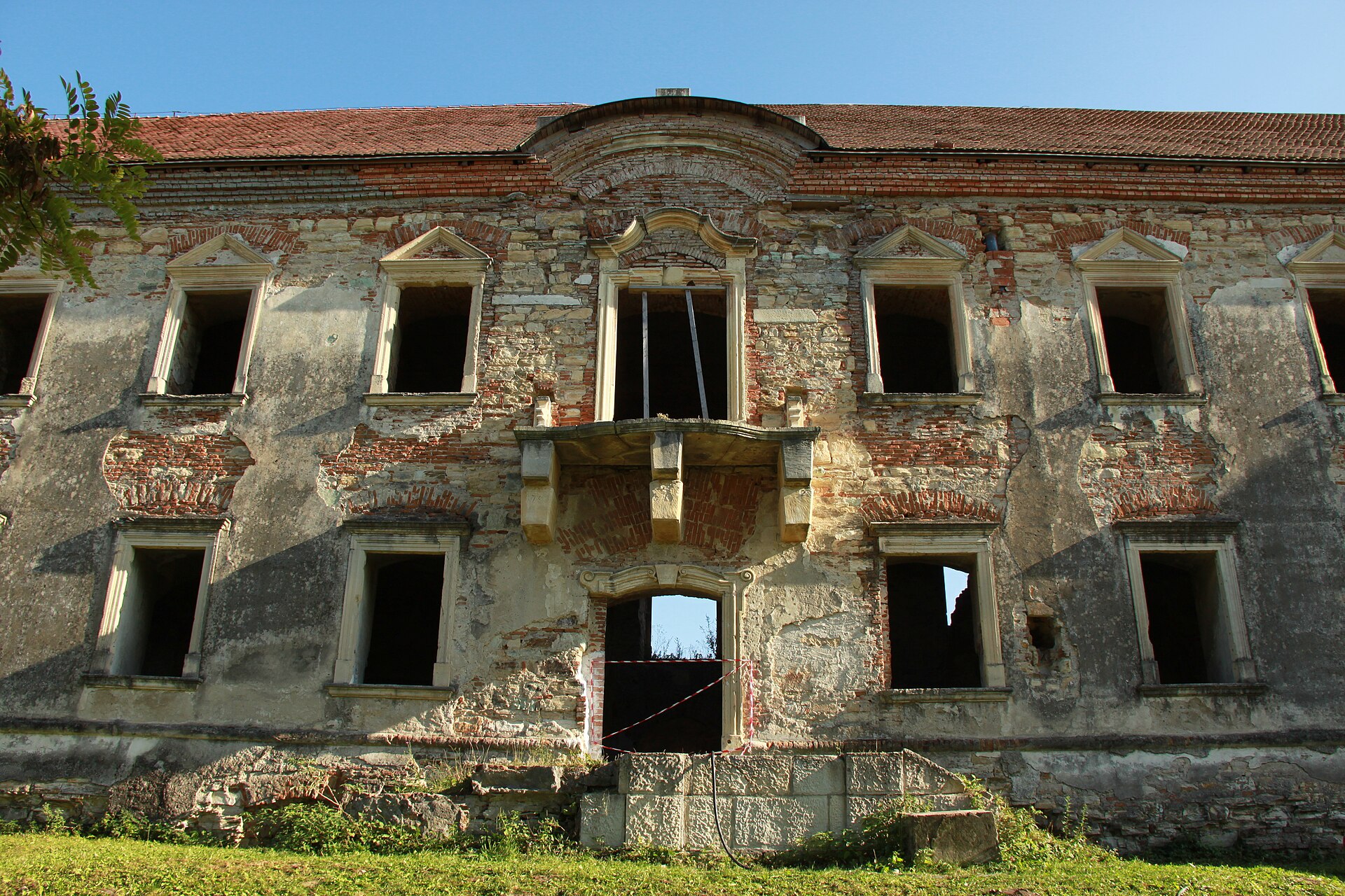 Fațada degradată cu fronton central, balcon și goluri de ferestre.
