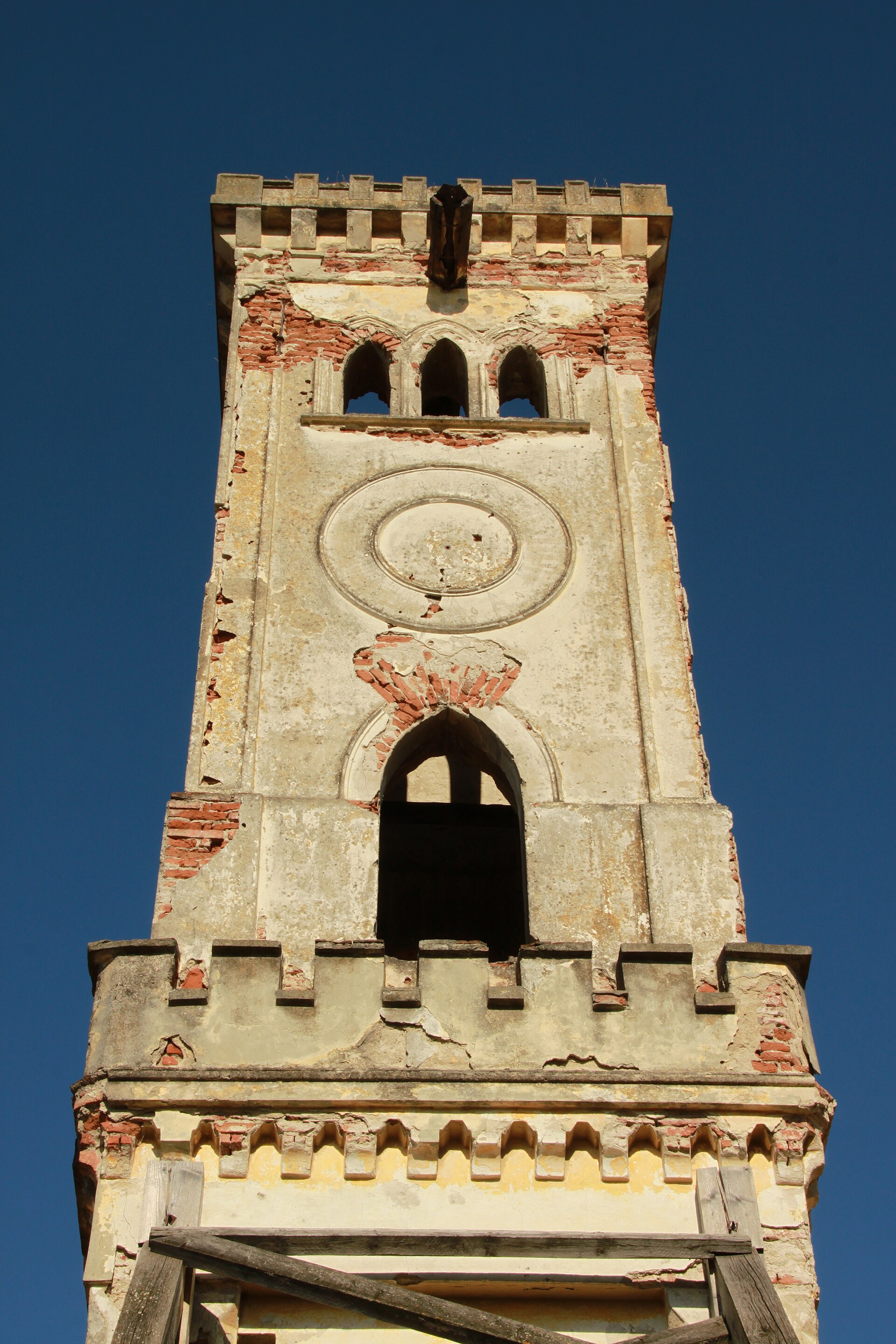 Partea superioară a turnului neogotic: creneluri, goluri și ornament circular.