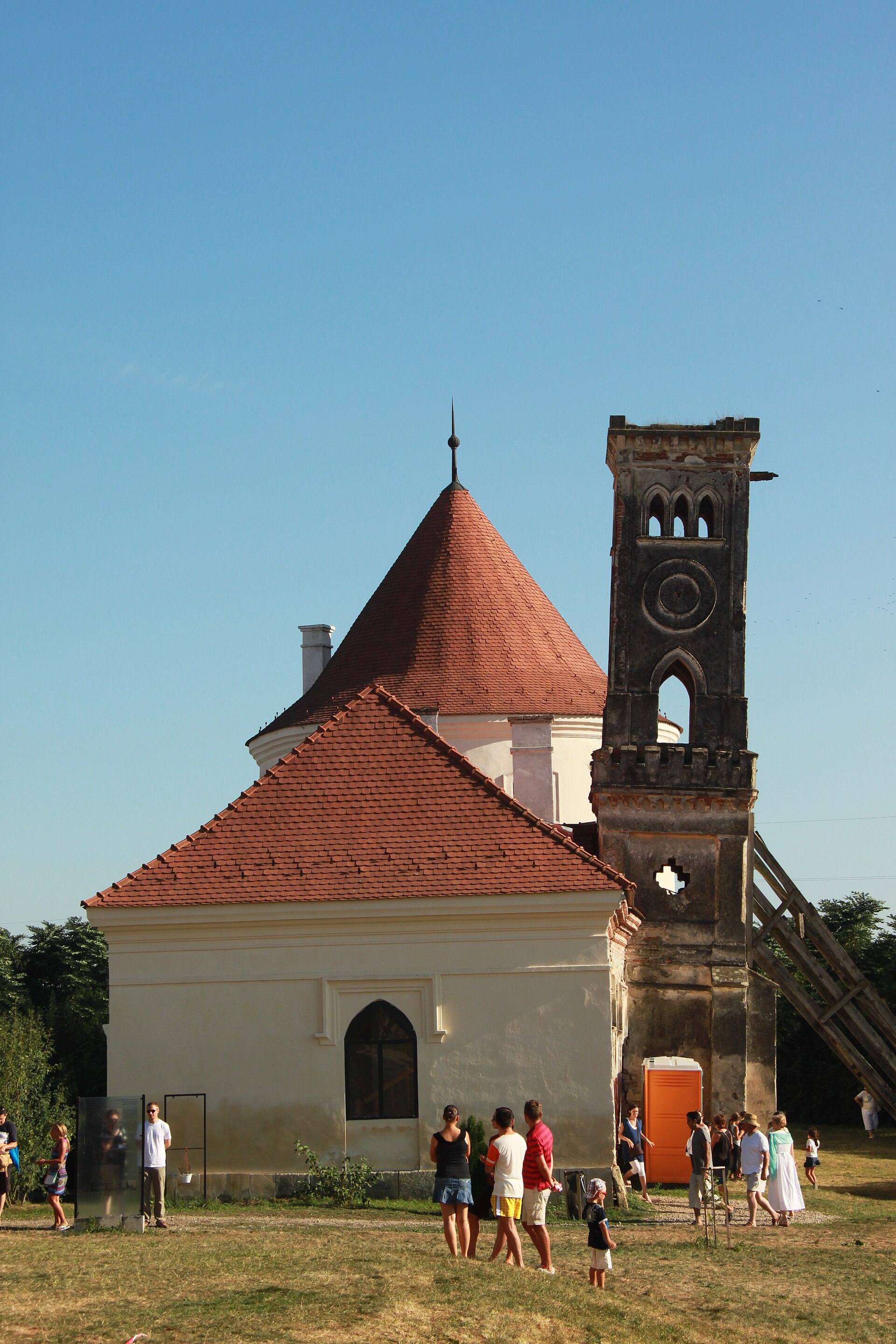 Fațada scurtă a anexei restaurate, acoperișul și turnul neogotic în fundal.