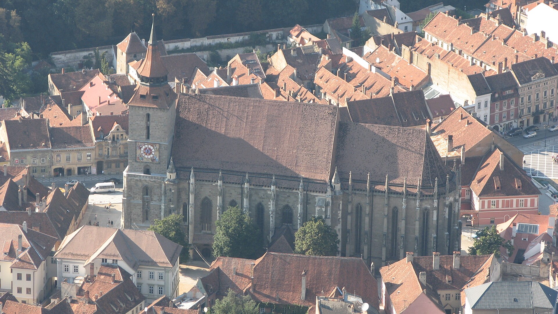 Biserica văzută de pe Tâmpa: acoperiș, turn și racordul corului, cu orașul în jur.