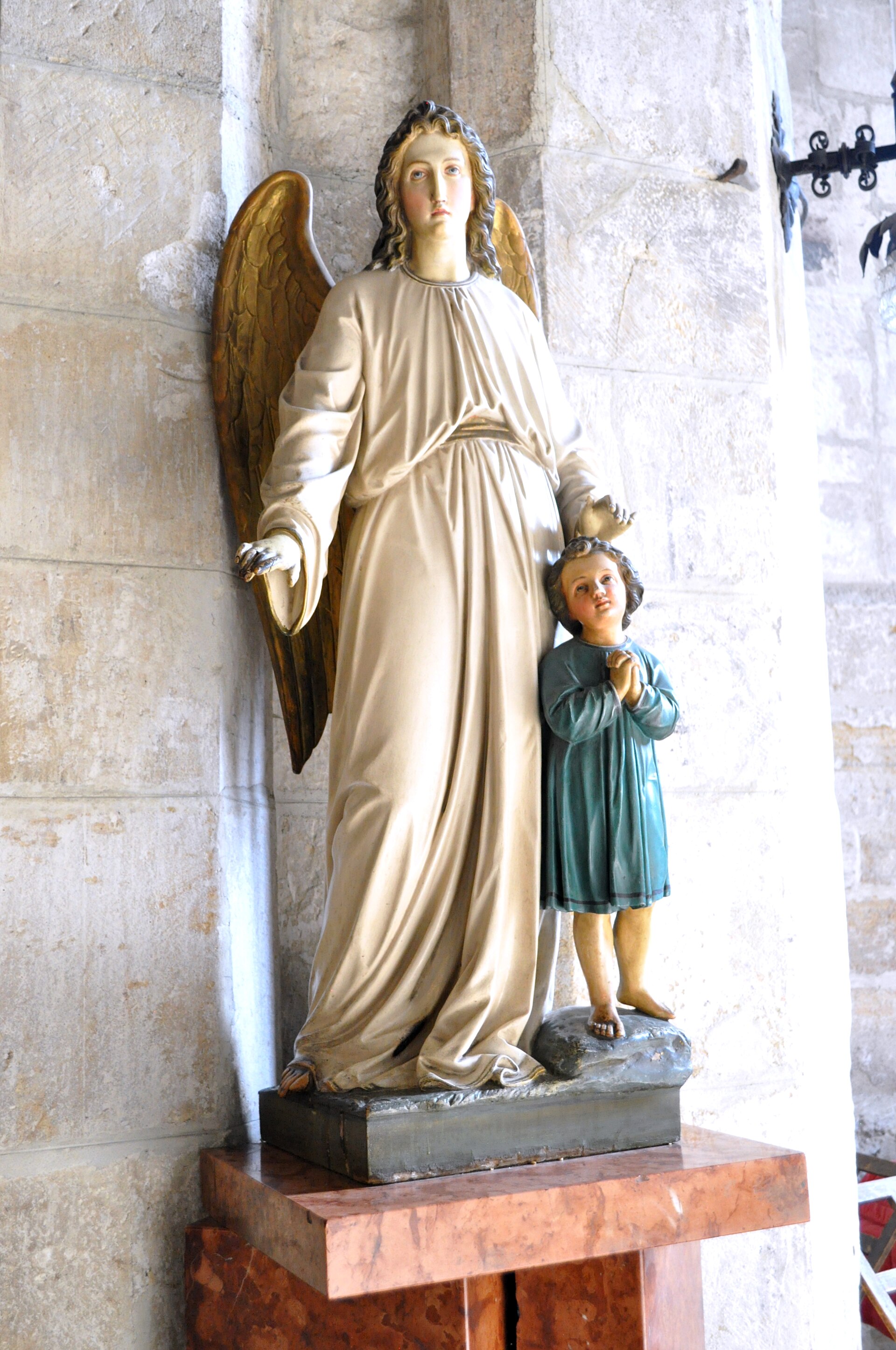 Statuie de interior și soclu, lângă zidăria de piatră.