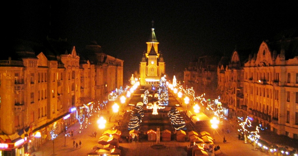 Vedere ridicată nocturnă de-a lungul Pieței Victoriei spre catedrală, mică în fundal; nu este vedere aeriană apropiată.