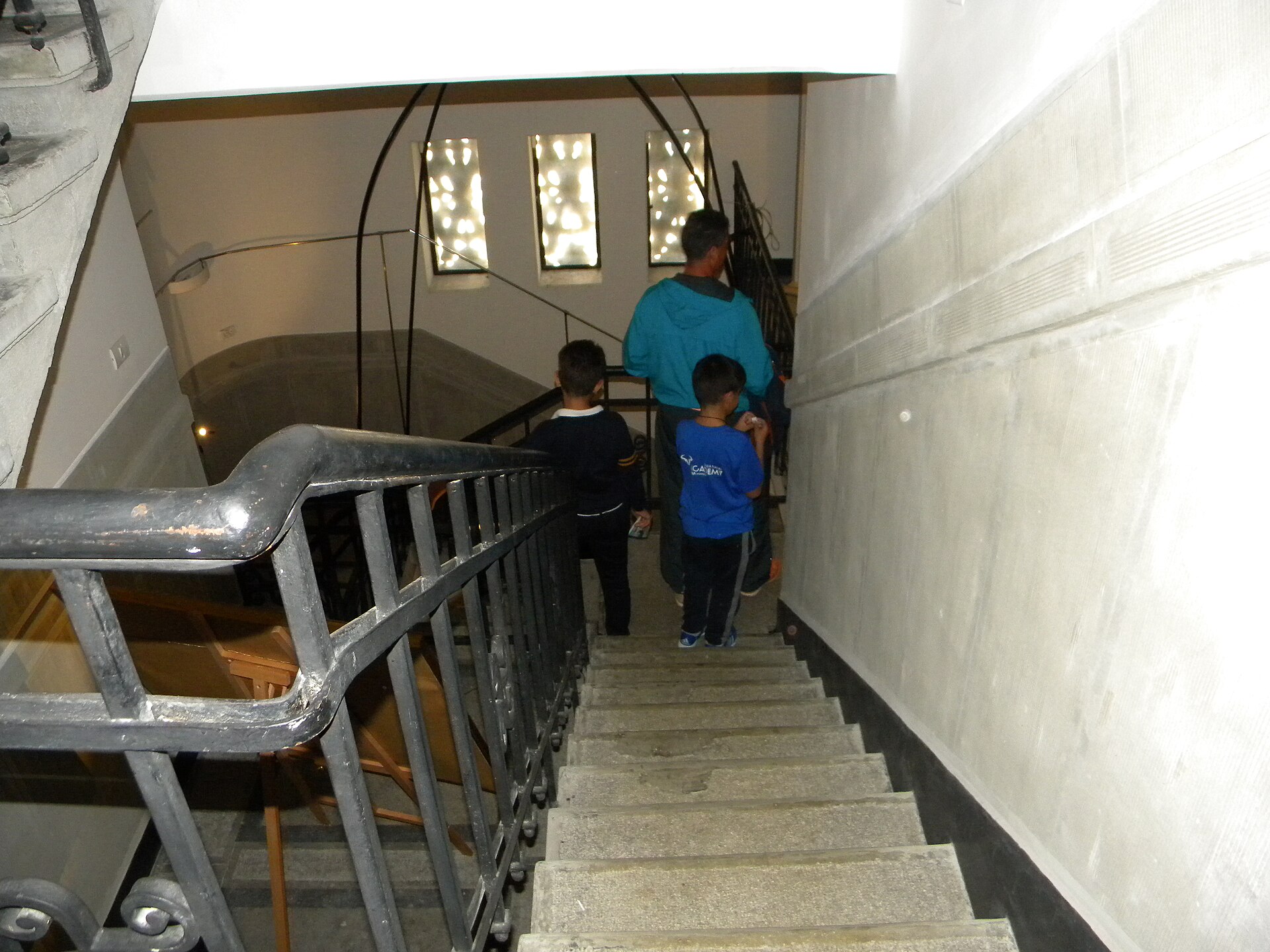 Trepte, balustradă, ziduri și fereastra unui podest; vizitatorii ascund o parte din scară.