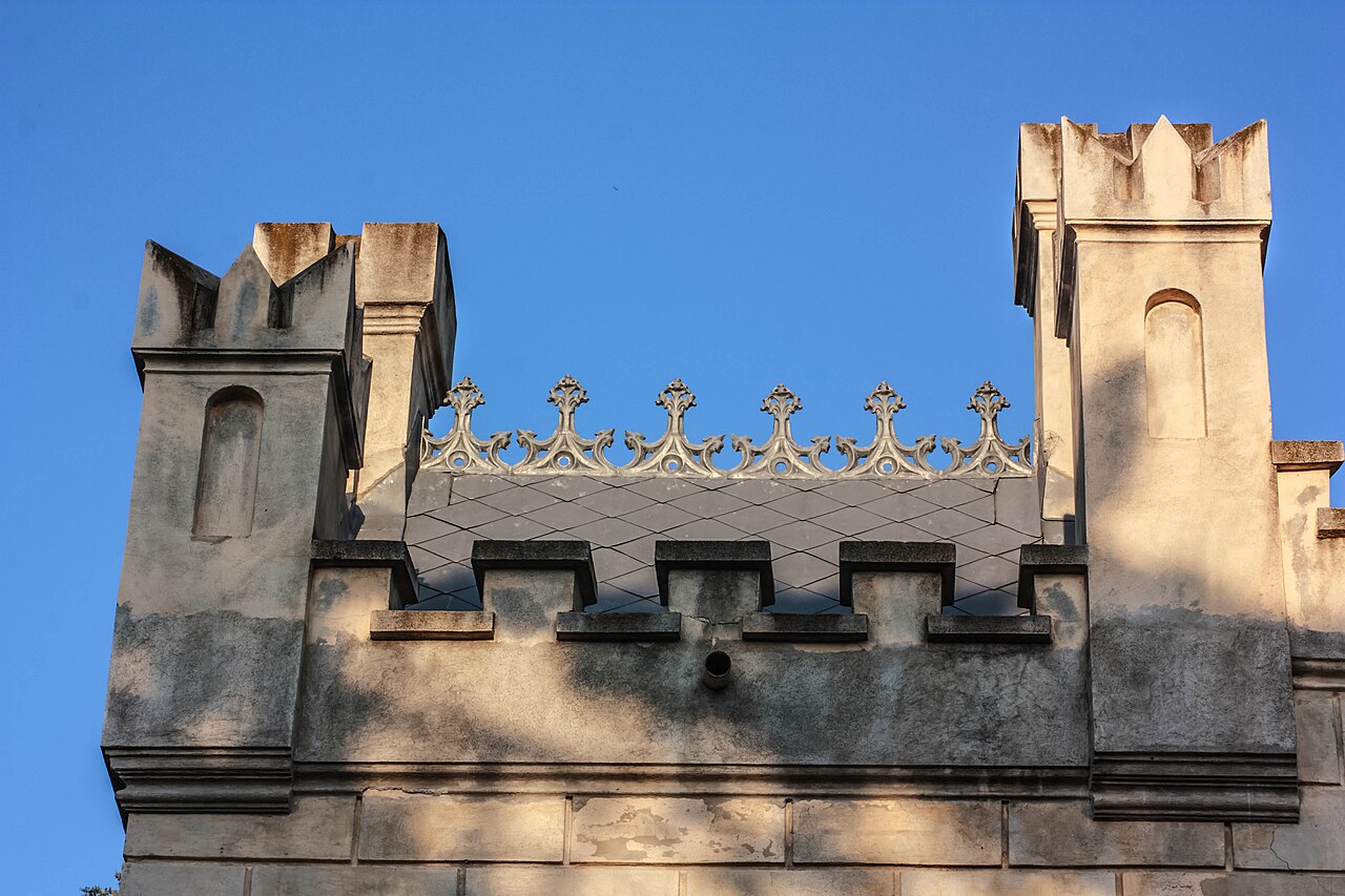 Coronament crenelat între două turnulețe, privit de la sol.