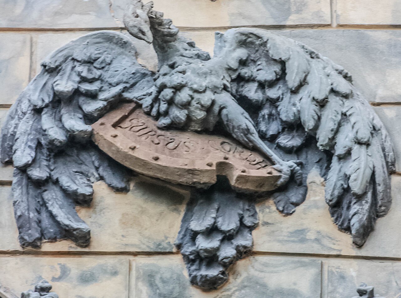 Relief cu aripi desfăcute și banderolă inscripționată.