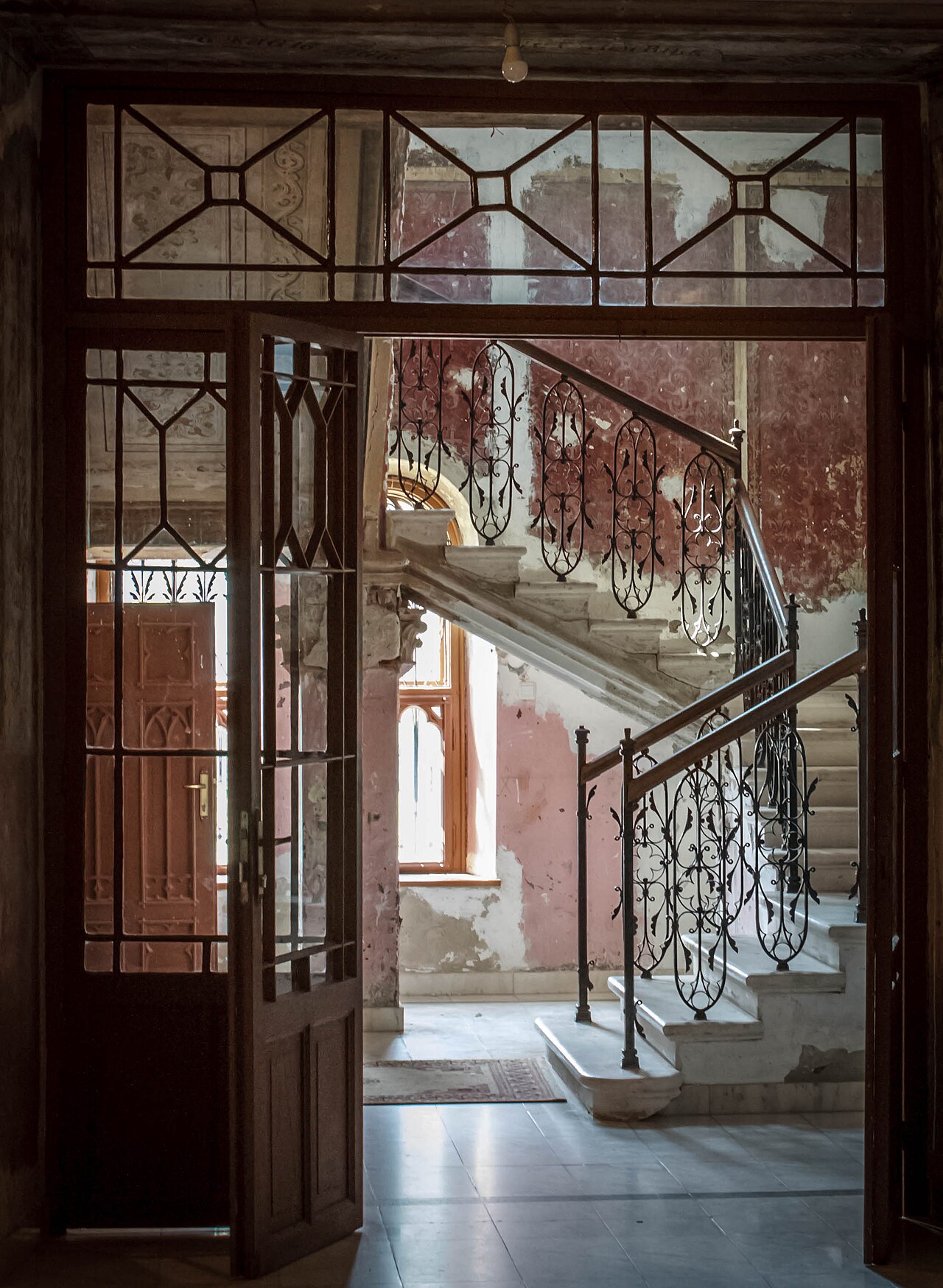 Ușă vitrată și vedere spre scara interioară cu balustradă metalică.