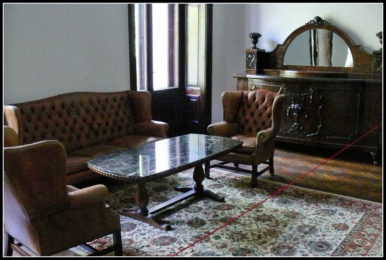 Salon cu mobilier, ferestre înalte și covor, vedere spre colț.