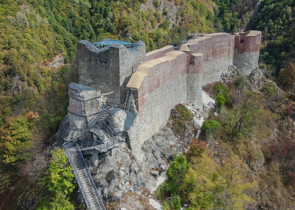 Vedere aeriană oblică spre donjon, pasarelele și turnurile de pe muchia stâncii.