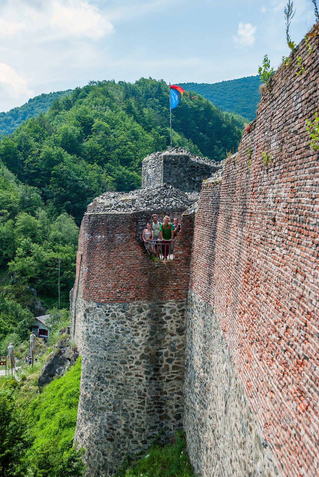 Curtină și turnuri semicirculare văzute oblic din apropiere, cu zidăria de cărămidă lizibilă.