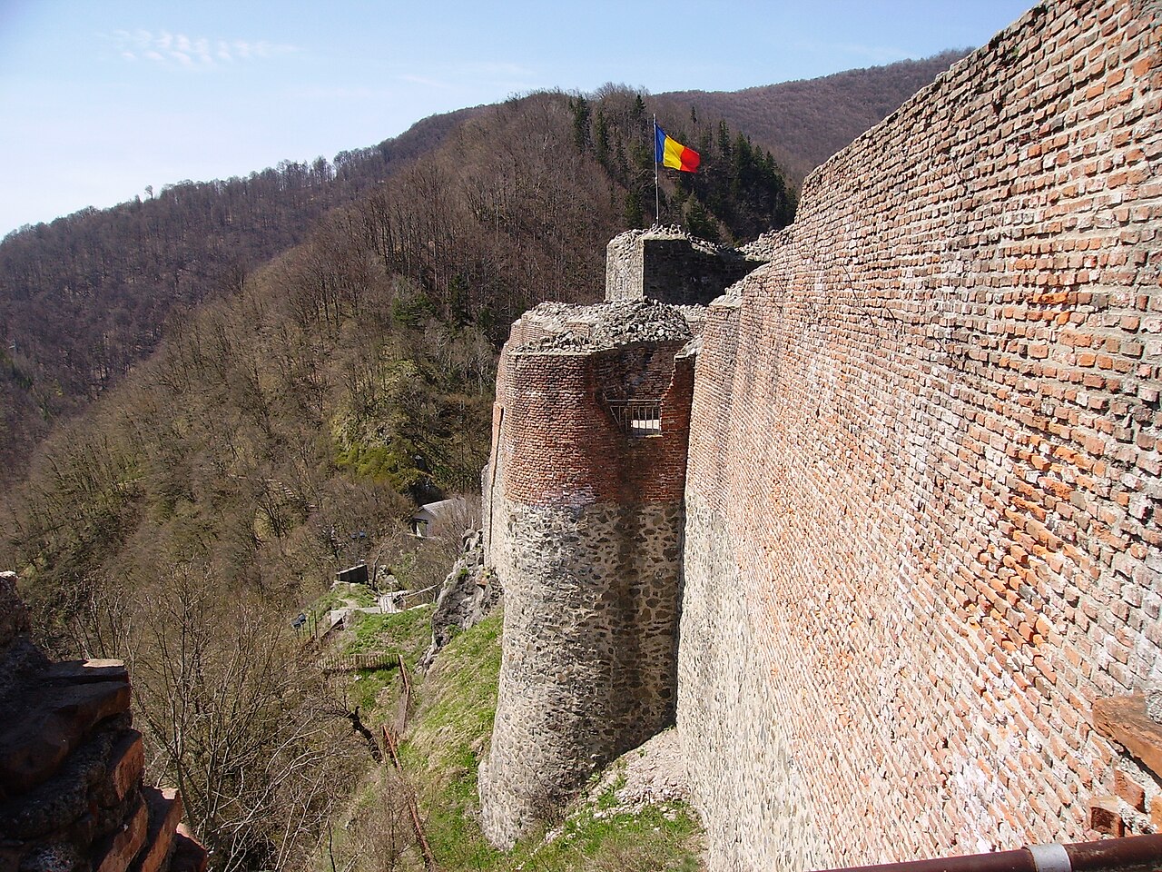 Turnuri semicirculare și zidul lung văzute din cetate, contrast între piatră și cărămidă.