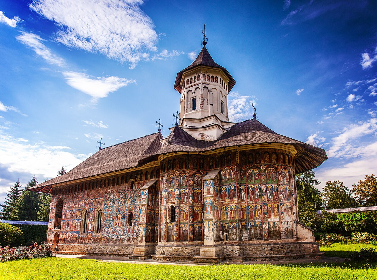 Biserica Buna Vestire văzută oblic: absidă, fațadă pictată, turlă și acoperiș.
