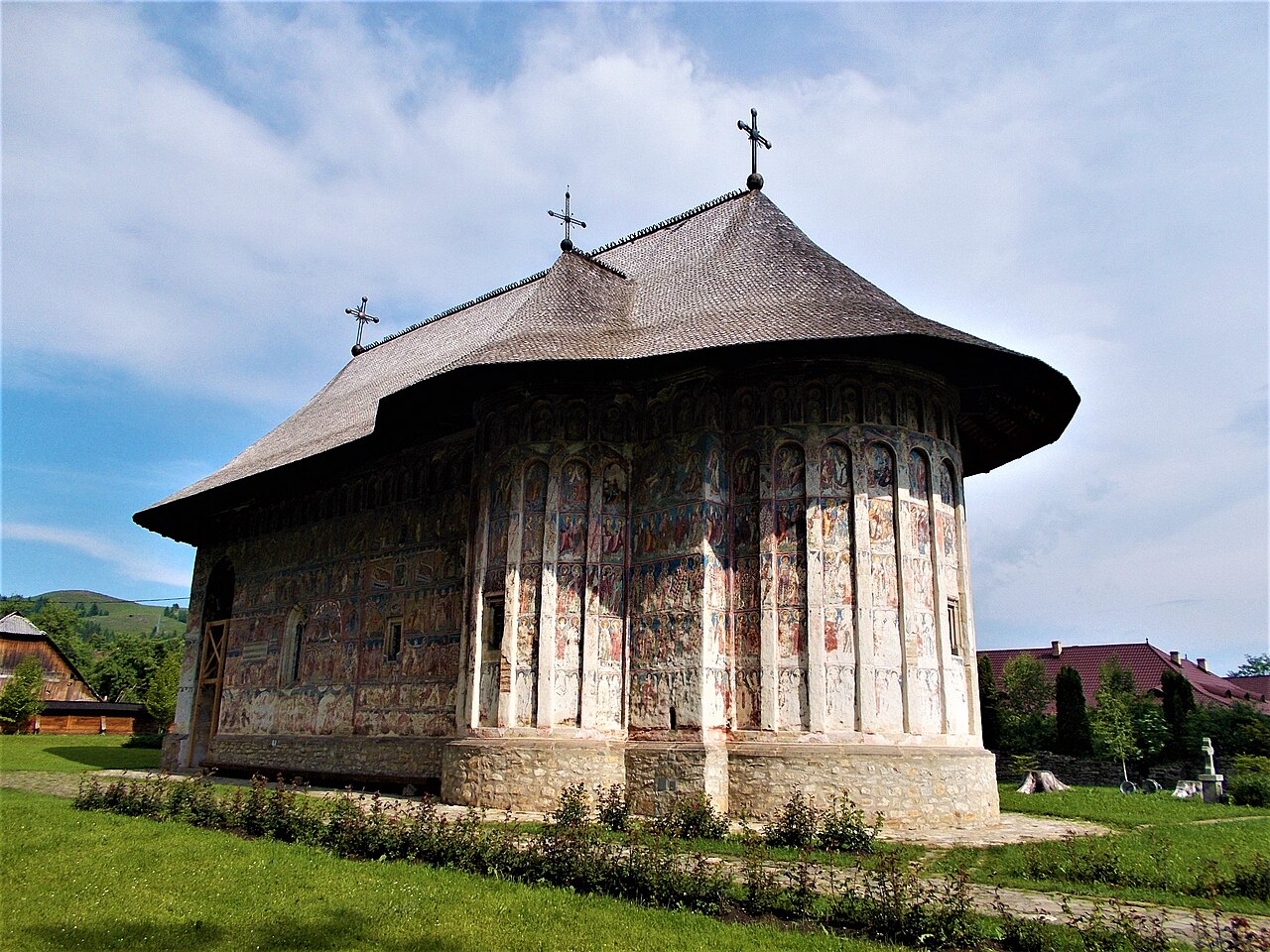 Biserica istorică văzută oblic: fațadă pictată, absidă și învelitoare fără turlă.