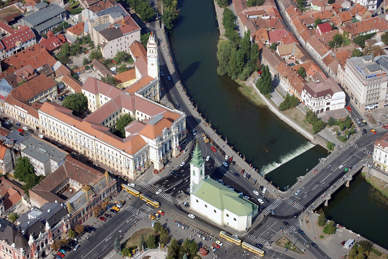 Vedere aeriană oblică: acoperișuri, aripi, curtea interioară și turnul palatului; biserica vecină este în prim-plan.