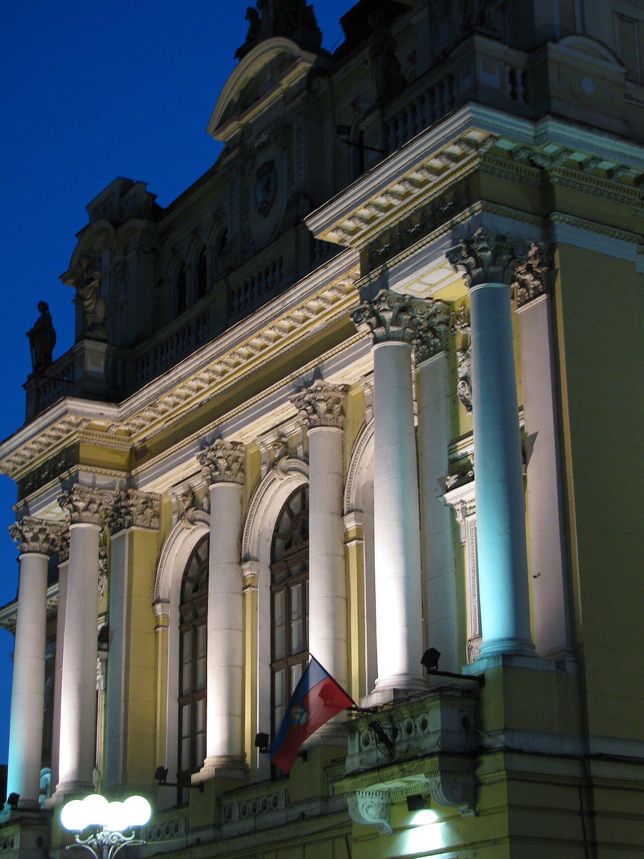 Coloanele, ferestrele înalte și balconul corpului central, în contraplonjeu nocturn.