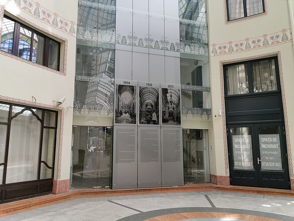 Perete al pasajului cu vitrine, decor și placă comemorativă.