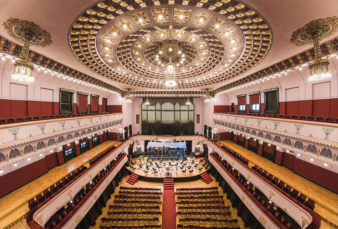 Sala de concerte fotografiată din zona înaltă a balconului: scenă, balcoane și plafon.
