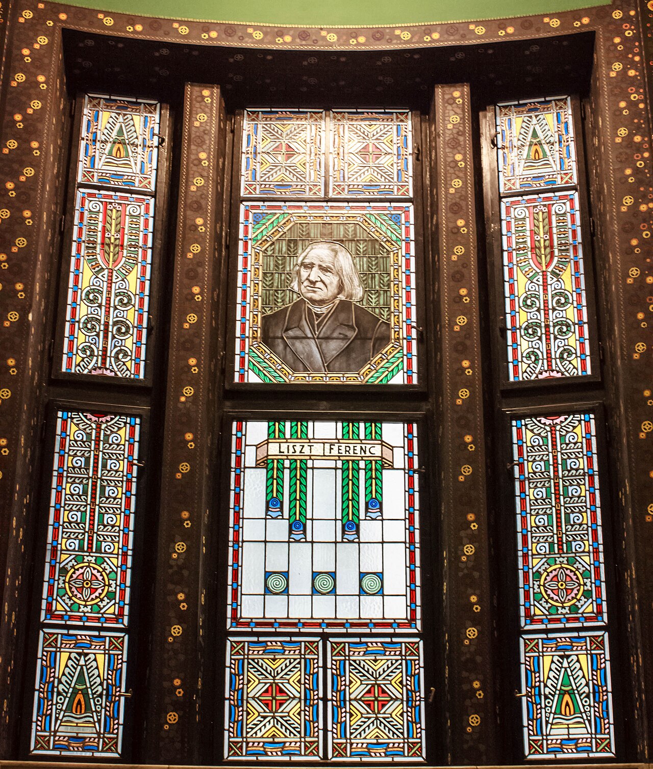 Vitraliu interior cu portret central și panouri decorative laterale.