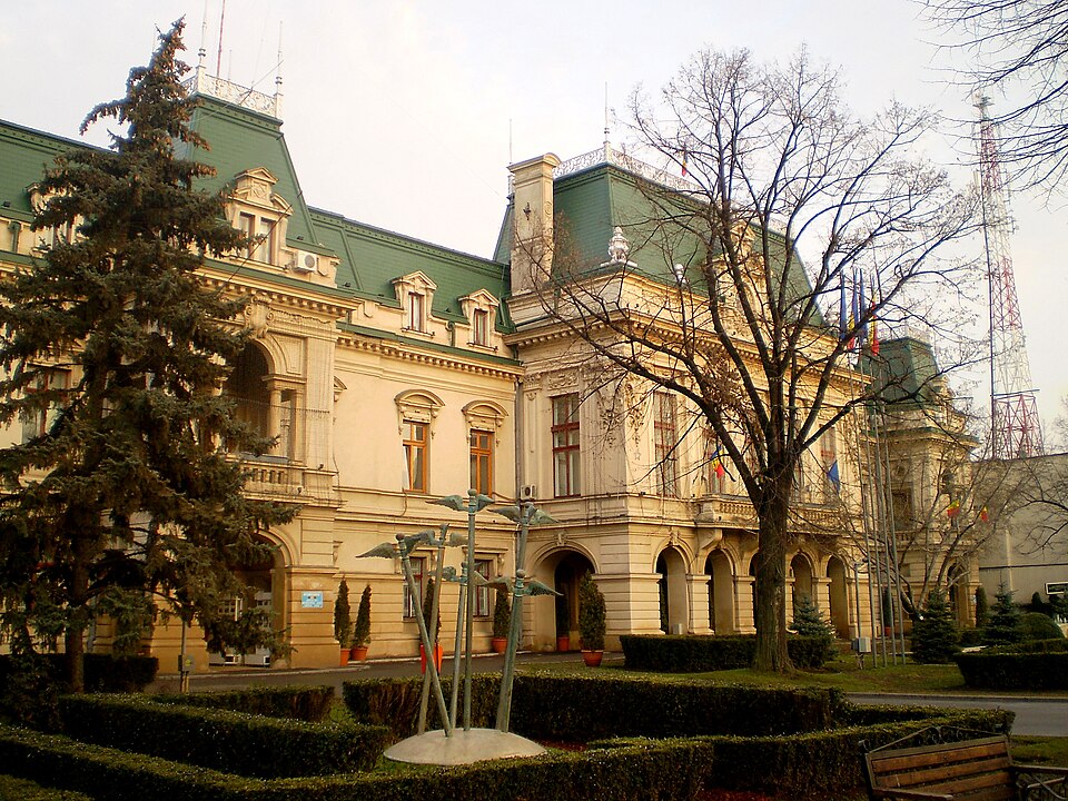 Colțul fațadei și porticul, privite oblic prin grădina din față.