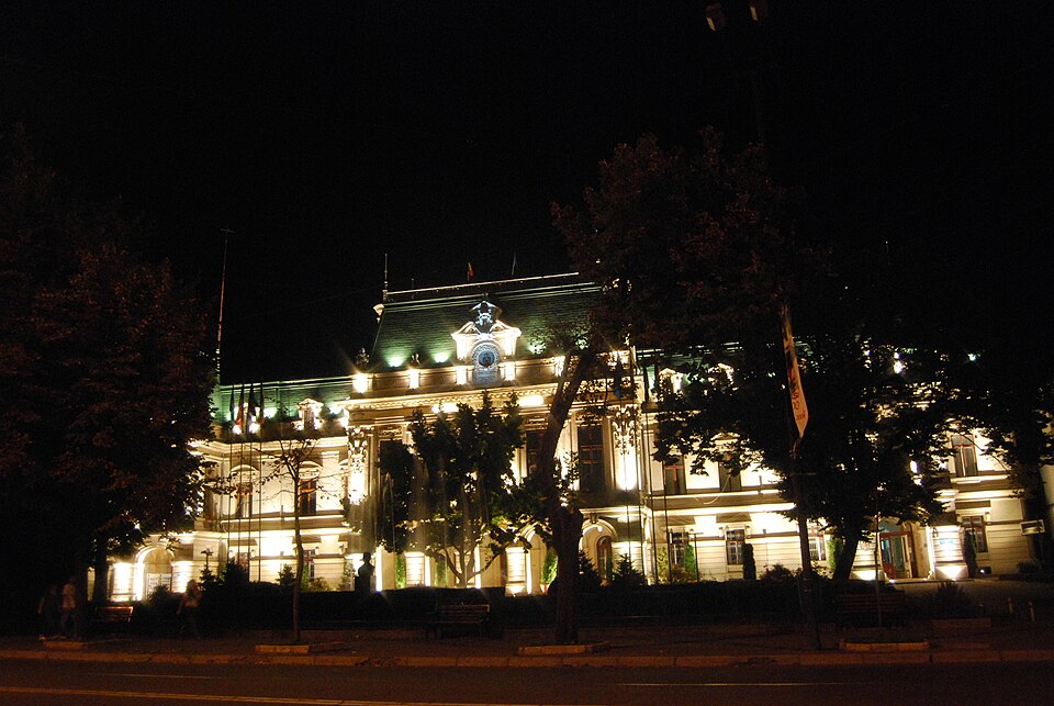 Fațada iluminată noaptea; referință pentru accentele volumetrice, nu pentru culoarea materialelor.