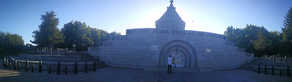 Panoramă frontală a teraselor și portalului; lumina de apus reduce lizibilitatea.