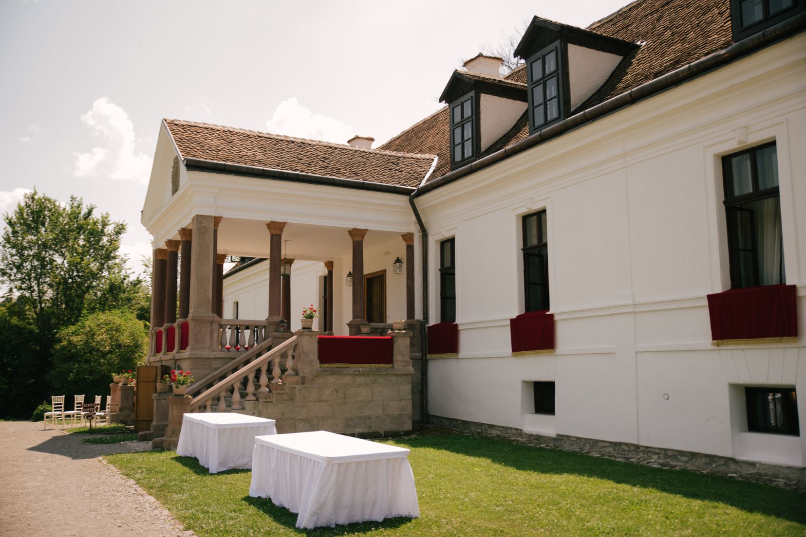Porticul și fațada laterală văzute oblic; mese de eveniment în curte.