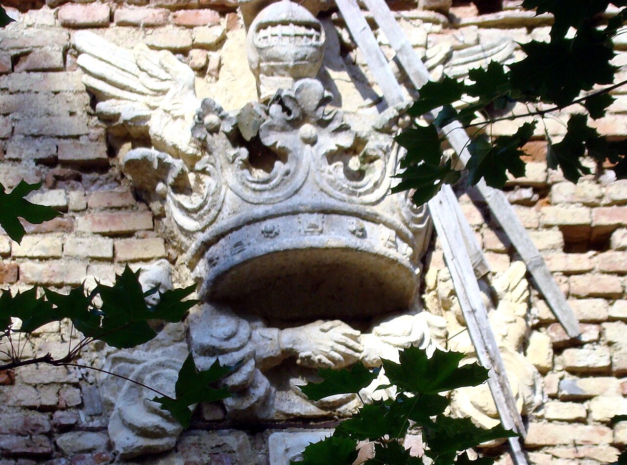 Blazon sculptat în piatră, cu tencuieli degradate în jur.