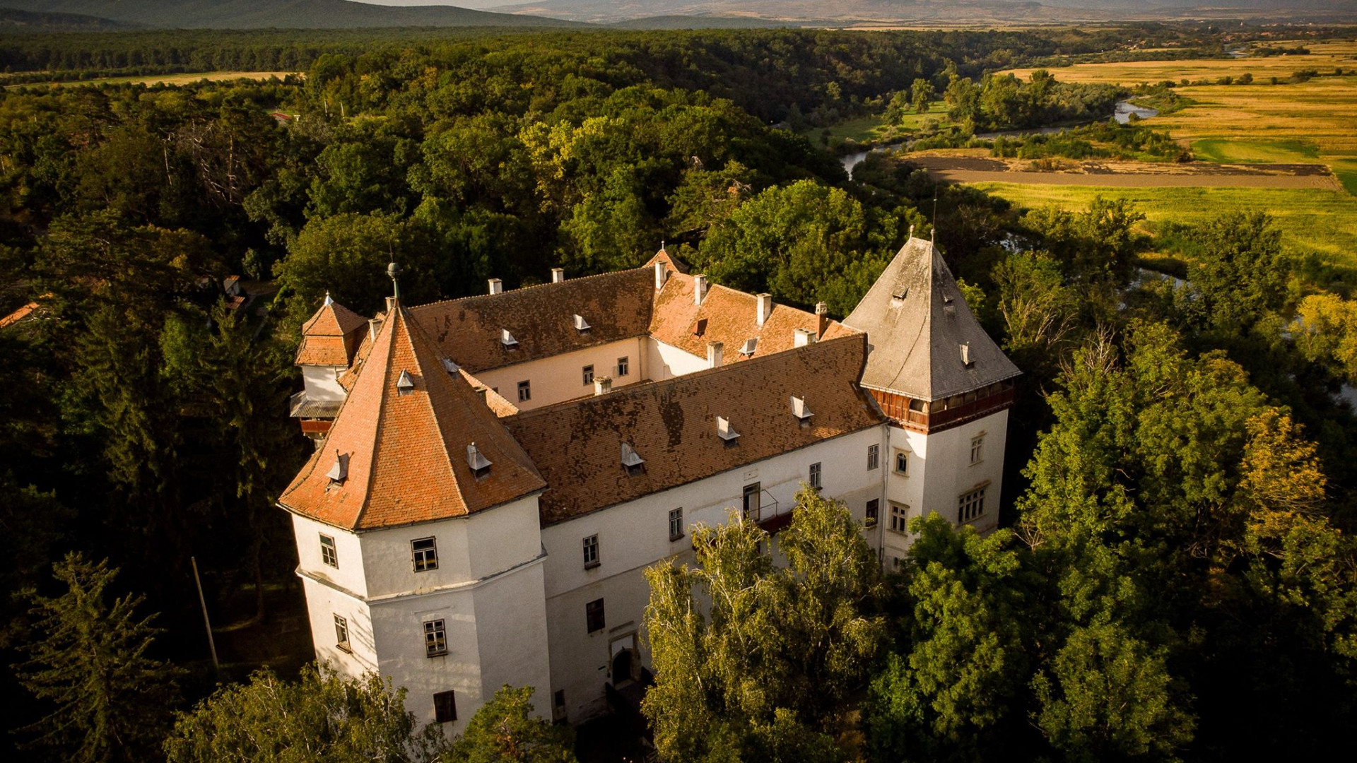 Fotografie aeriană oblică a castelului: turnuri, acoperișuri, curte și parc.