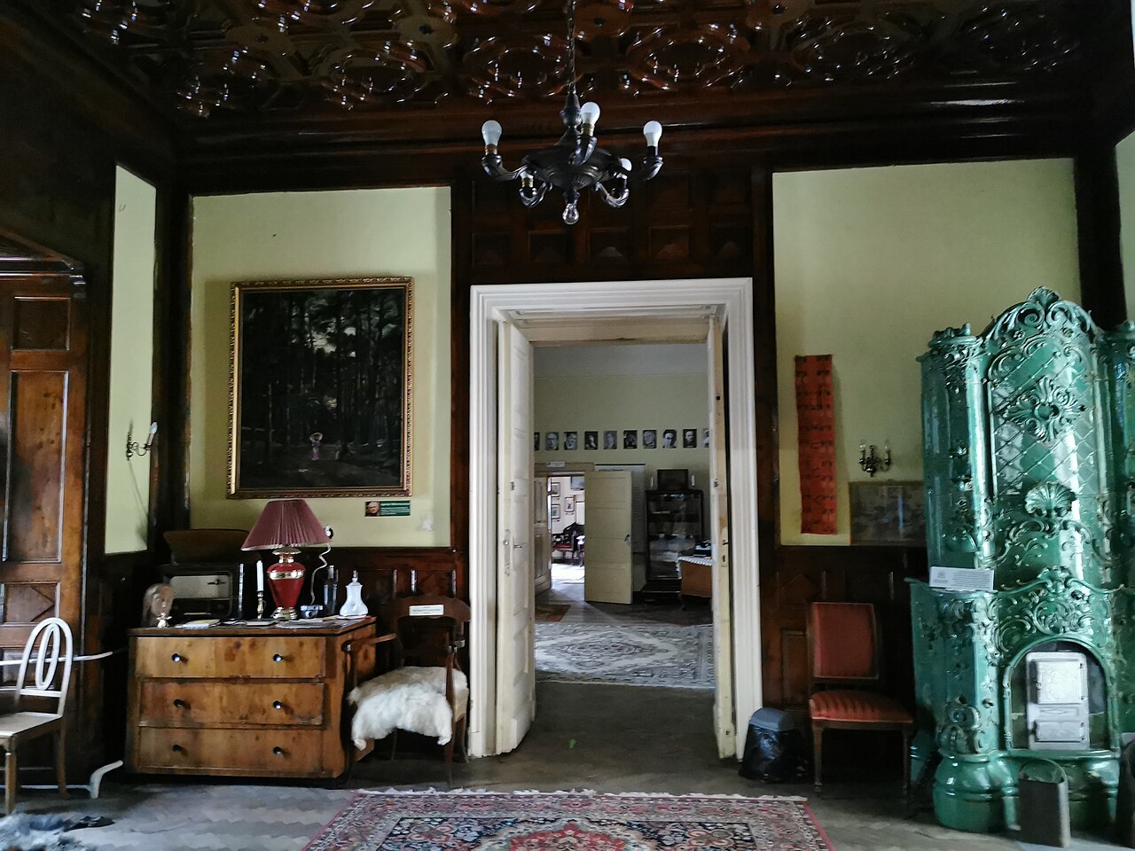 Sală cu tavan decorat, sobă verde și uși către încăperi succesive.