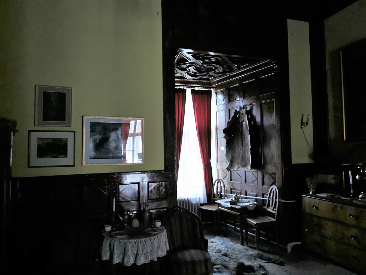 Salon cu tavan casetat și ferestre, în lumină redusă.