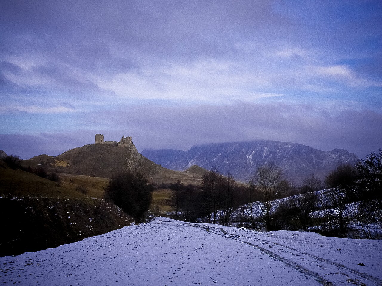 Cetatea pe culme în iarnă, cu relieful și zidurile văzute de la sol.